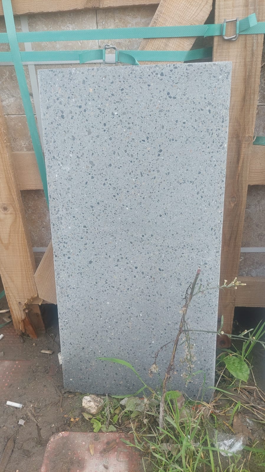 Koyu gri, küçük taş agregaları içeren 30x60 cm ebatlarında Terrazo zemin kaplama karosu. Palet üzerinde sergileniyor.