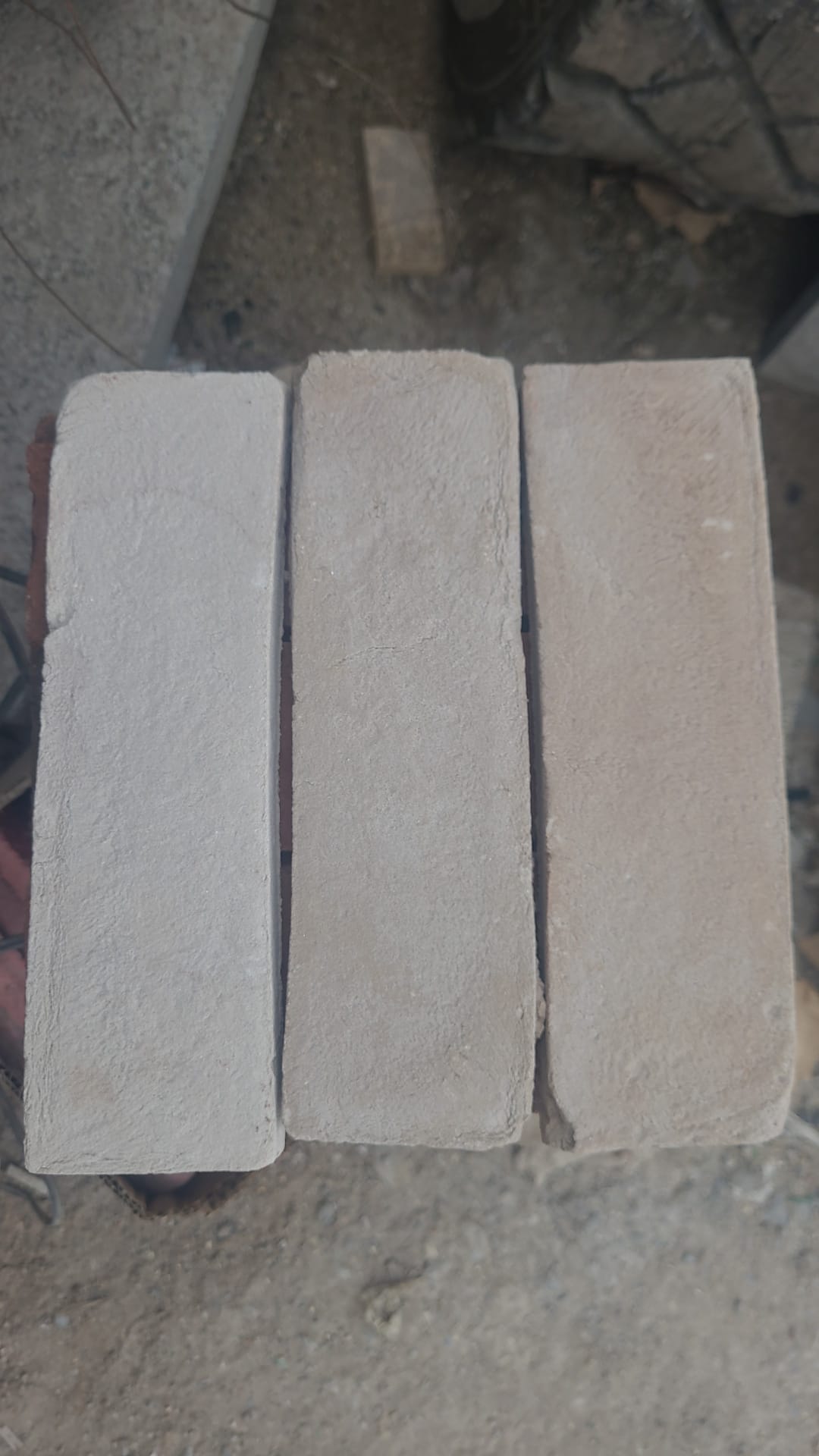 Üç adet yan yana dizilmiş, açık bej ve krem renkli, pürüzlü yüzeyli el yapımı dekoratif tuğla.